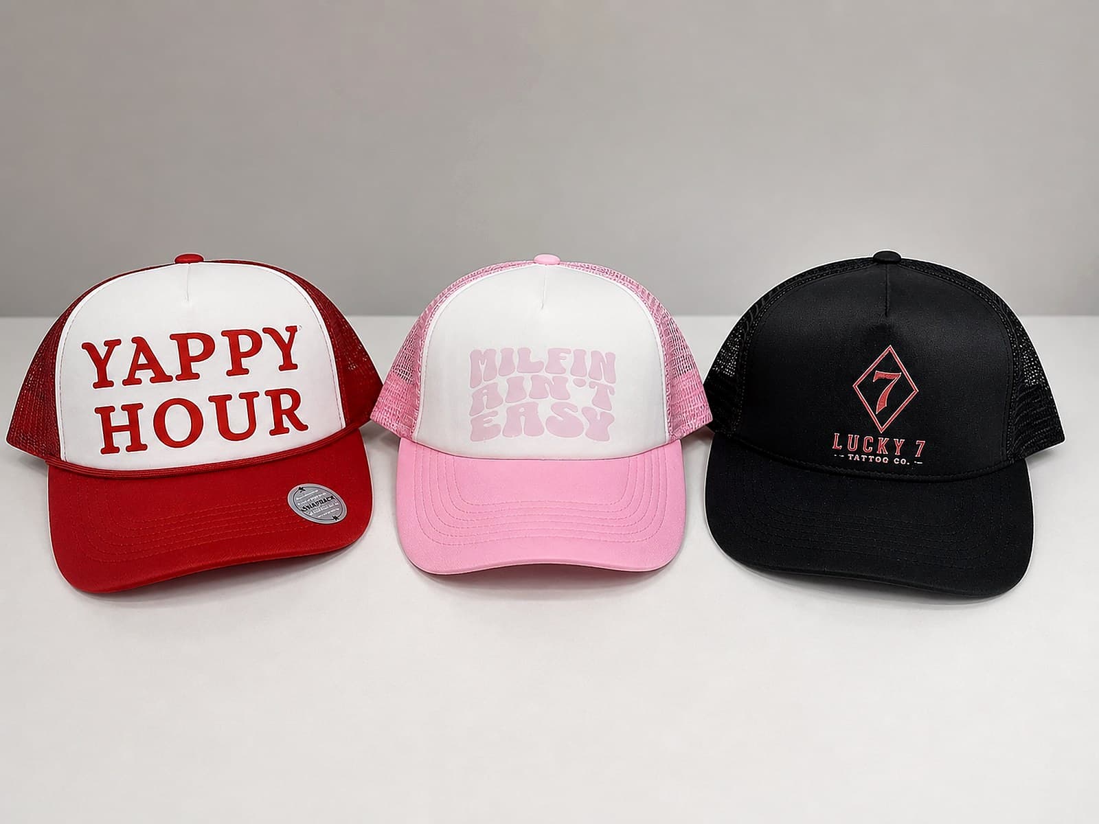Red, pink, and black custom trucker hats displayed in a row