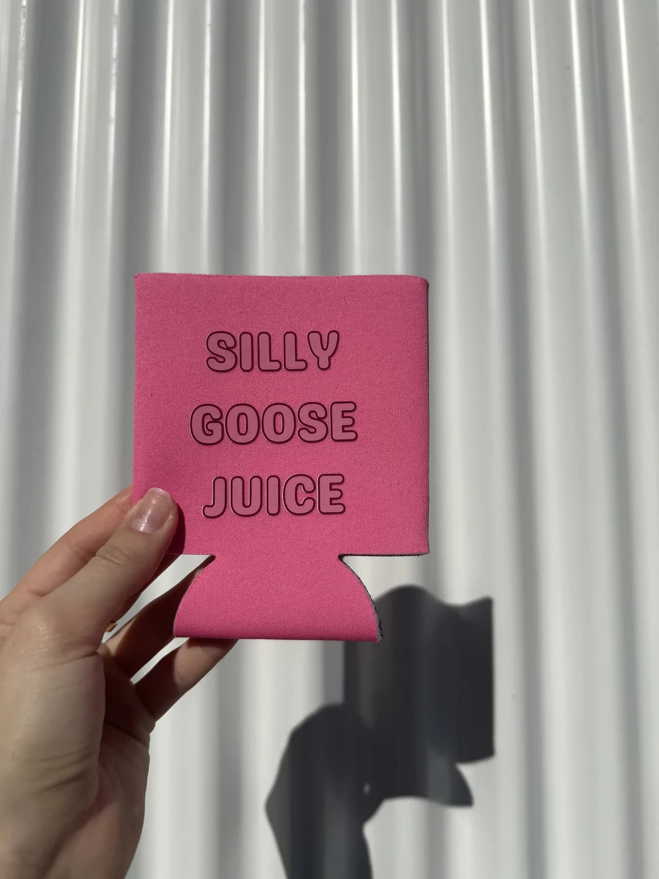 Bright pink custom Silly Goose Juice koozie held outdoors